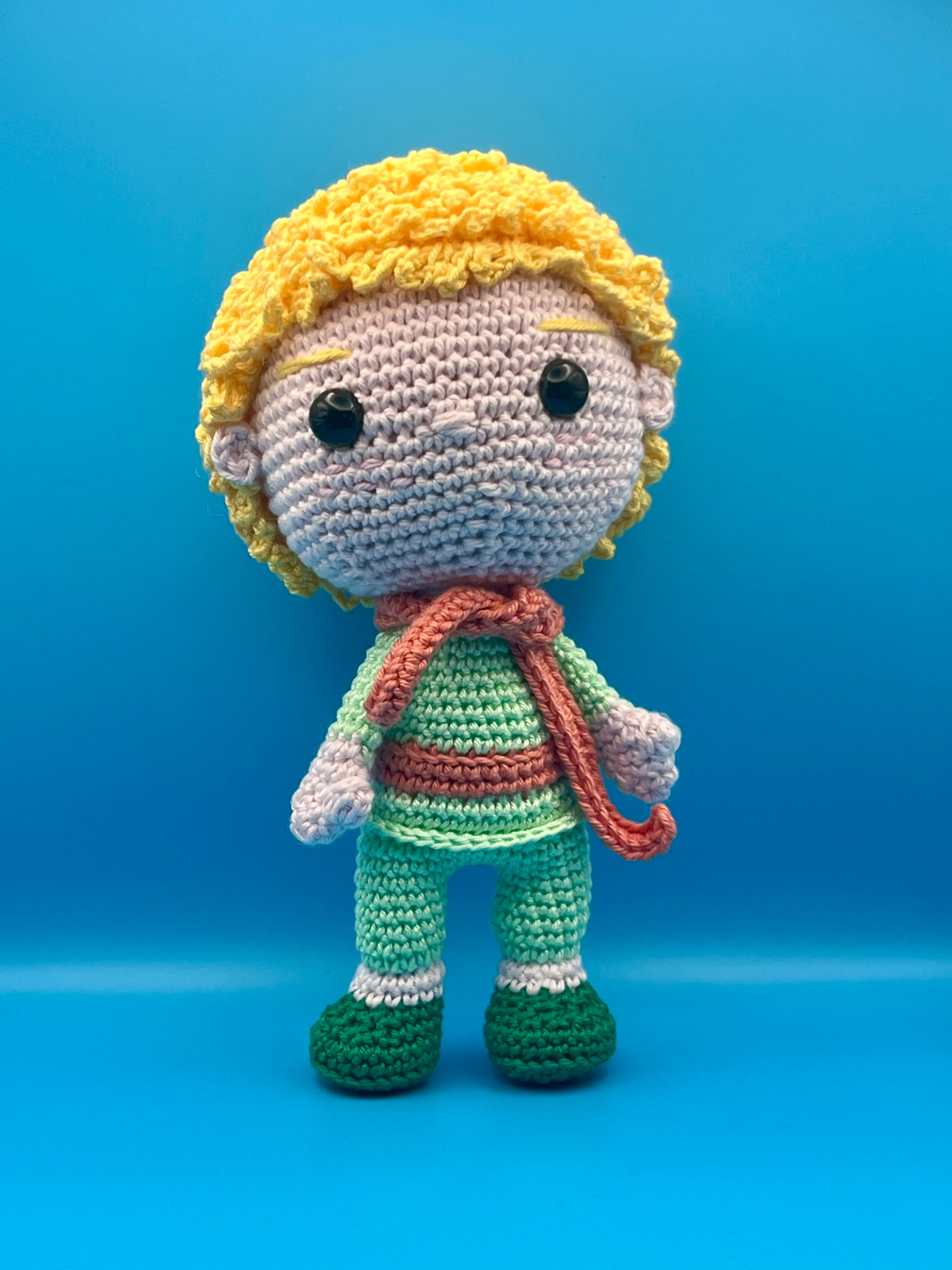 The Little Prince amigurumi posed against a blue storybook background