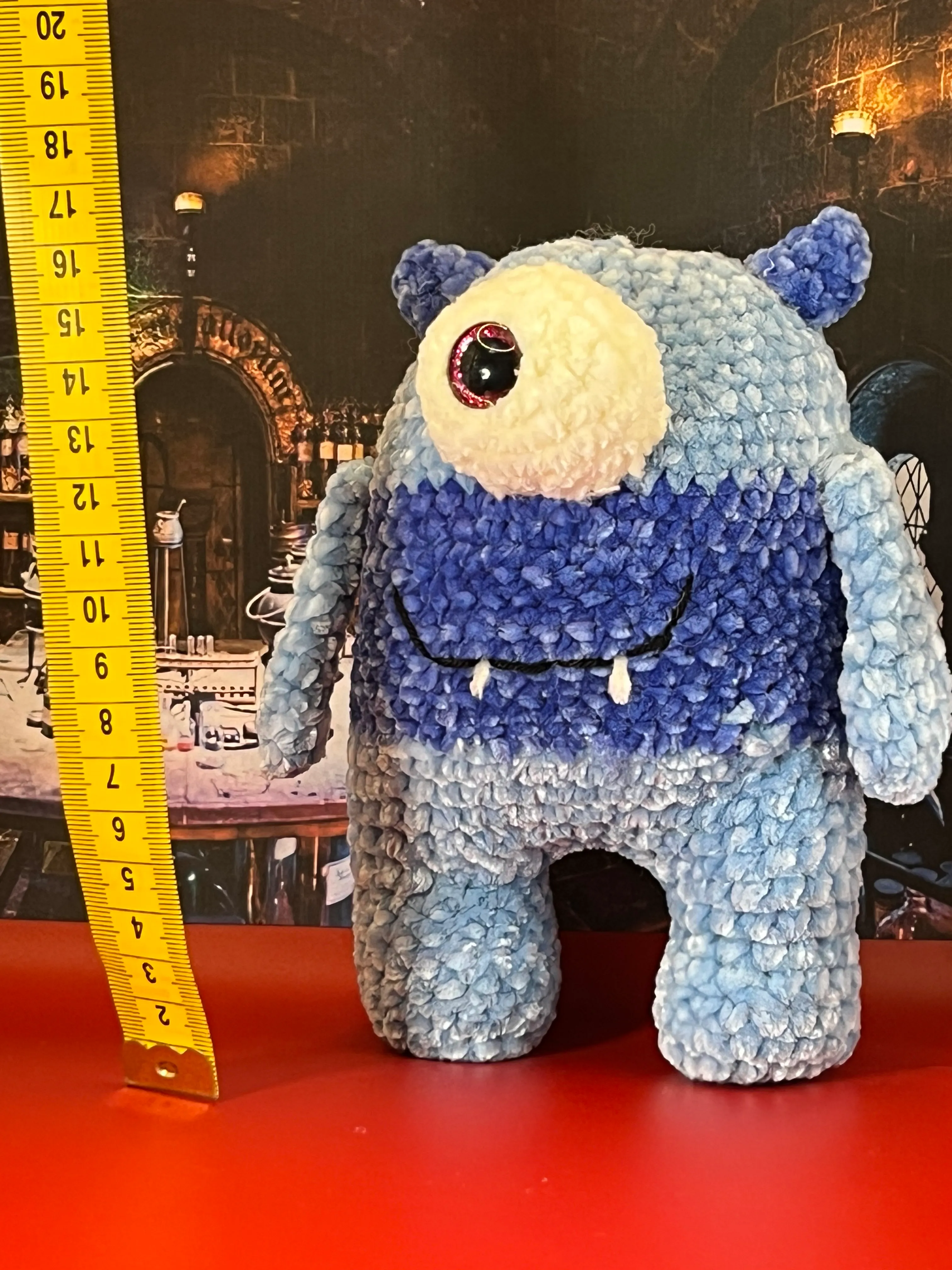 Blue cyclops amigurumi with white fangs in a fantasy laboratory setting
